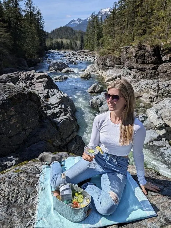 Megs with a gin cocktail on a riverside picnic blanket